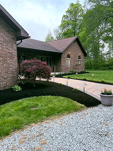 A brick home with a curved black mulch bed and a red Japanese maple beside a gravel drive.