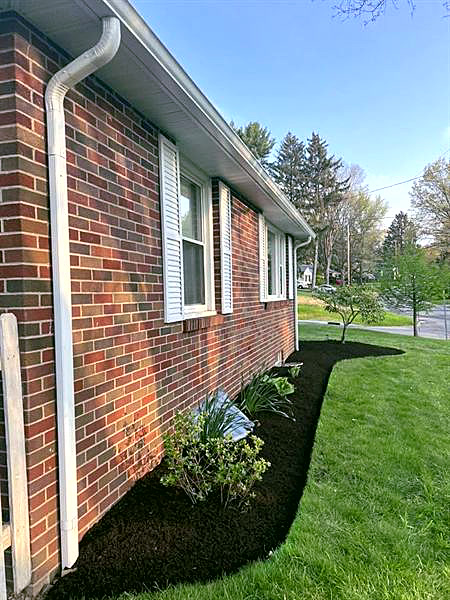 A brick ranch with a curved black mulch bed and new shrubs along the side.