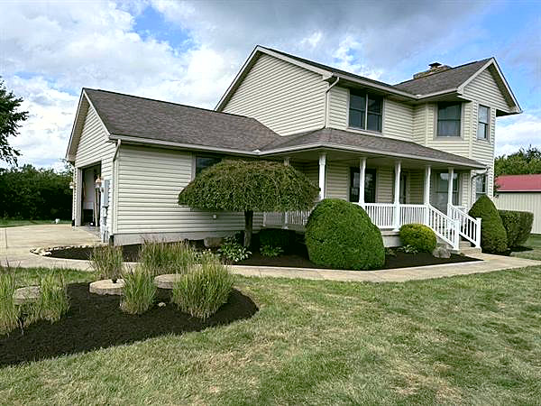A farmhouse with fresh black mulch beds and trimmed shrubs along the front.