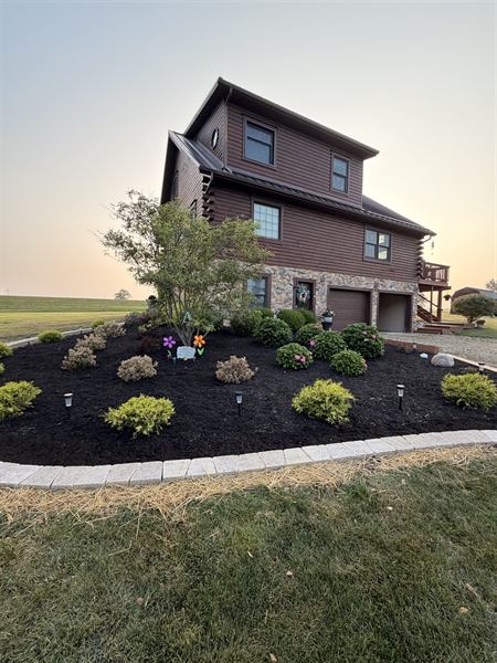 A log home at dusk with a wide black mulch bed of shrubs lit by low path lights.