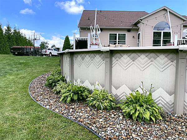 A river rock bed with hostas curving around an above-ground pool and deck.