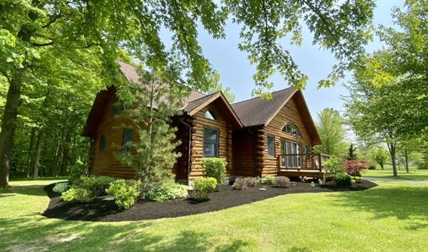 A log cabin with fresh mulch beds and trimmed shrubs under a canopy of trees.