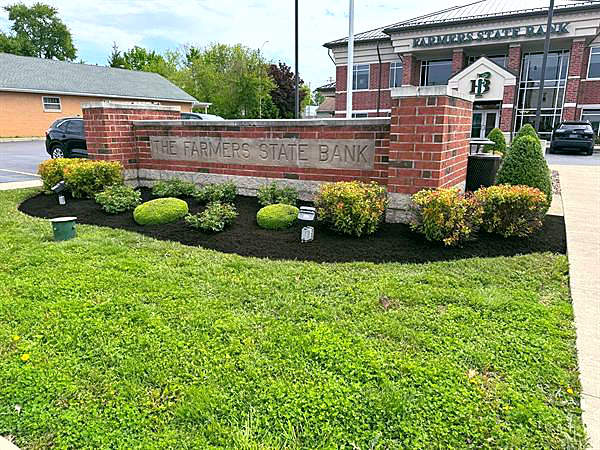 A brick bank sign surrounded by shrubs and fresh black mulch.