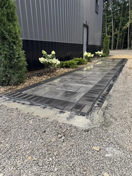 Looking down a long paver walkway with a dark soldier-course border, hydrangeas and evergreens beside it.