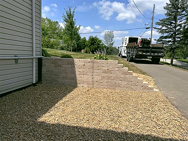 A tiered block retaining wall with built-in steps beside a house, filled with clean gravel.