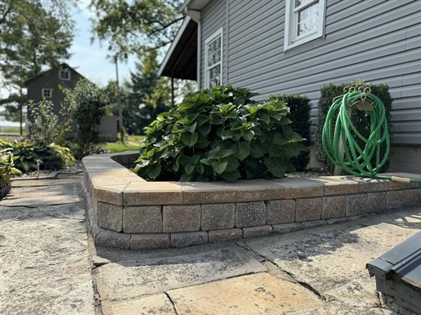 A curved block retaining wall forming a raised planter with a hydrangea, set in a flagstone patio.