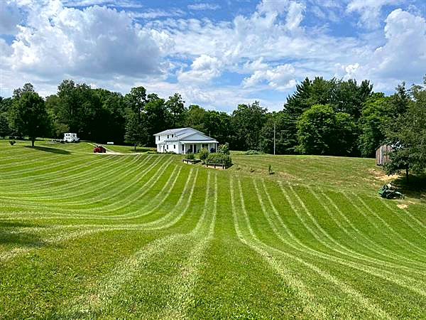 A striped lawn sweeping down a hillside toward a house.