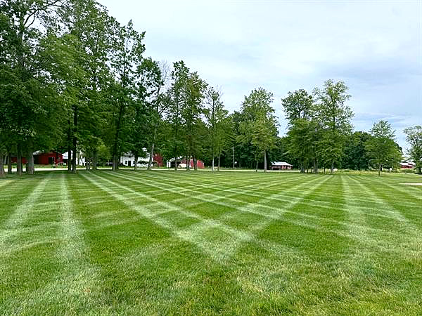 A large striped lawn with mature trees and a red barn in the distance.