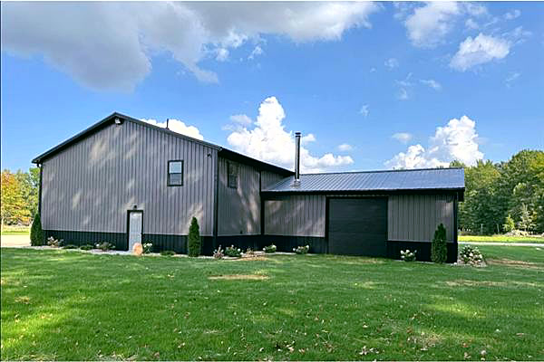A pole barn with a black wainscot and fresh plantings on a thick green lawn.