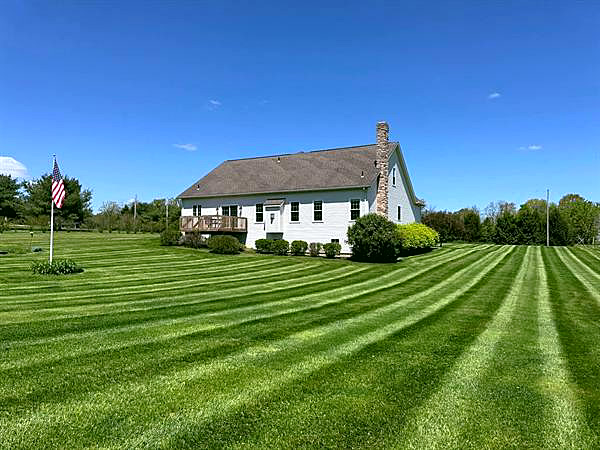A striped lawn in front of a white farmhouse with an American flag.