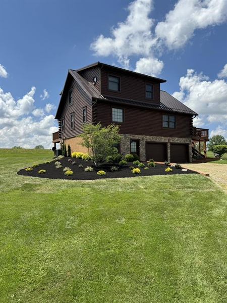 A dark log home with a fresh black-mulch foundation bed planted with shrubs and a young tree.