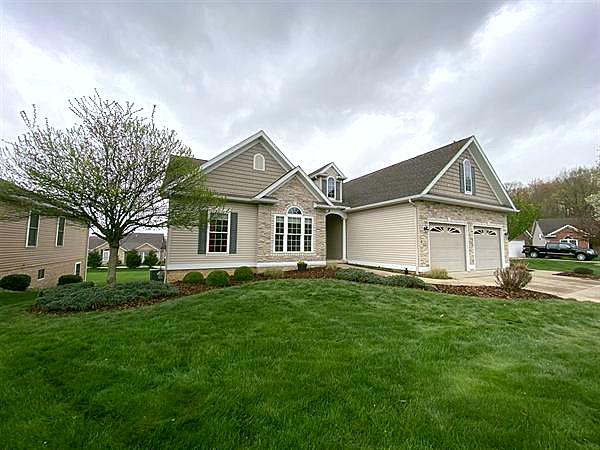A stone-front home with fresh mulch beds, new shrubs, and a trimmed lawn.